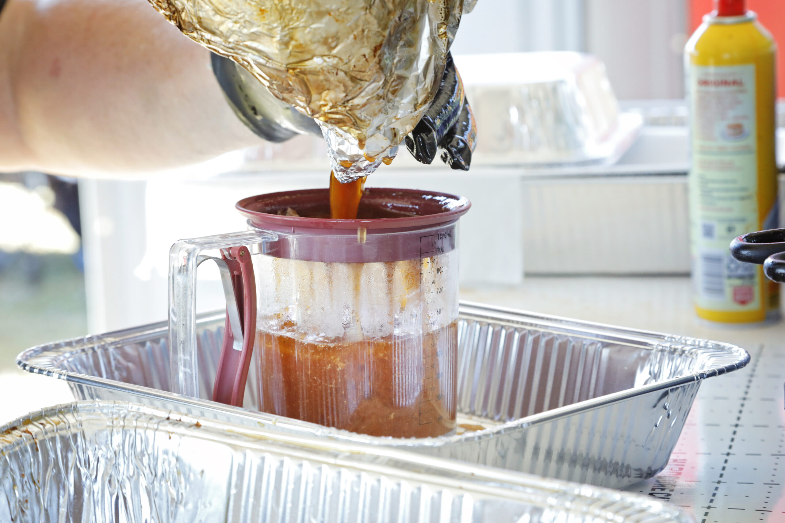 A hand pours sauce into a measuring cup.